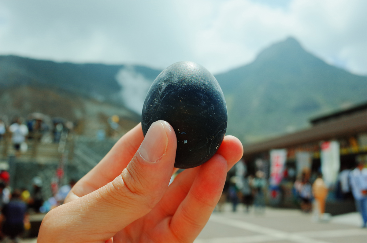 A black egg held in hand with Owakudani in background.