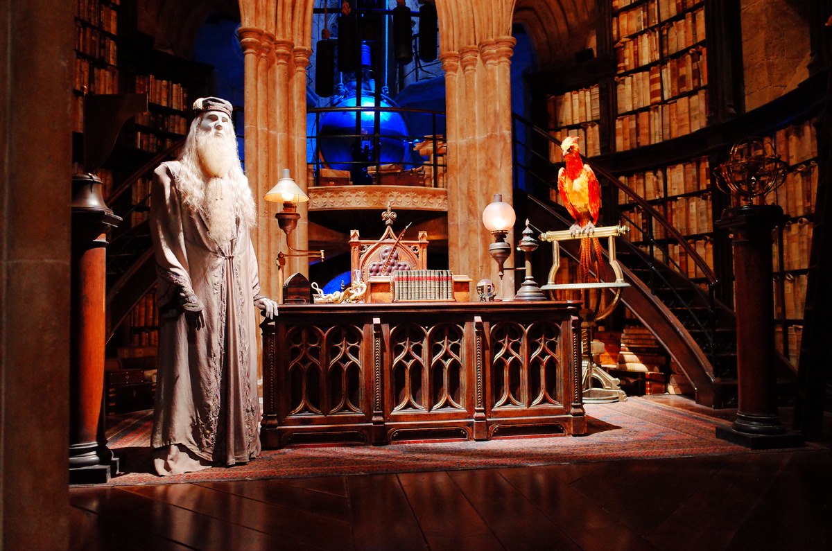 A mannequin of Dumbledore from Harry Potter rests a hand on a wood desk.