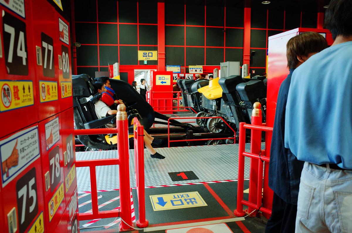 Red storage lockers in foreground with seated rider in background on Eejanaika at Fuji-Q Highland