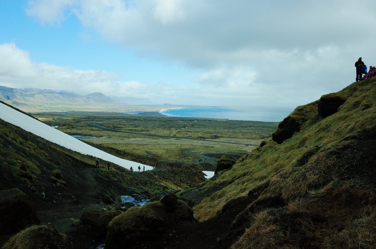 A person on a steep hill, surrounded by snow and distant mountains.