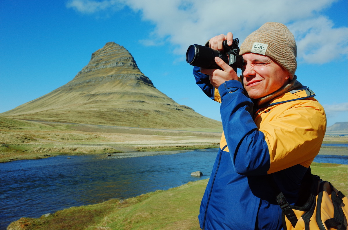 Photographer with yellow and blue jacket in front of Kirkjufell in Iceland.