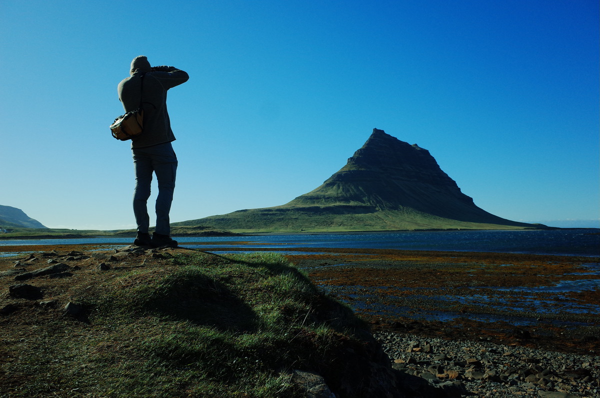 A photographer with a camera with the mountain Kirkjufell in the background.