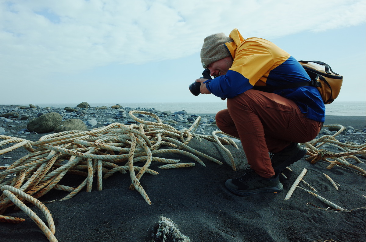 Person photographing tangled rope in sand near a beach.