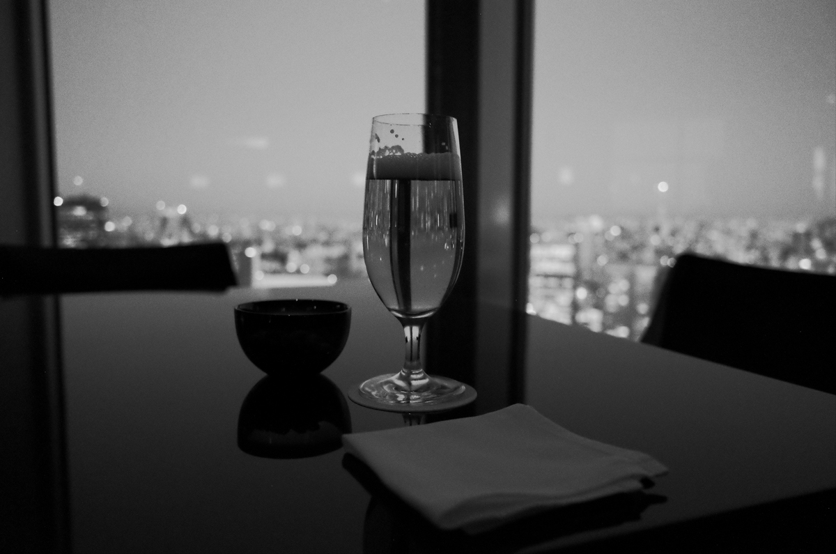 Glass of beer next to a bowl of nuts on a table.