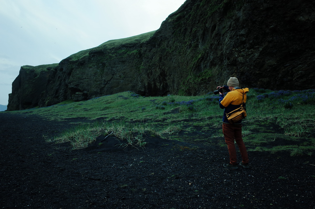 Photographer standing next to a moss covered mountain with camera in hand.