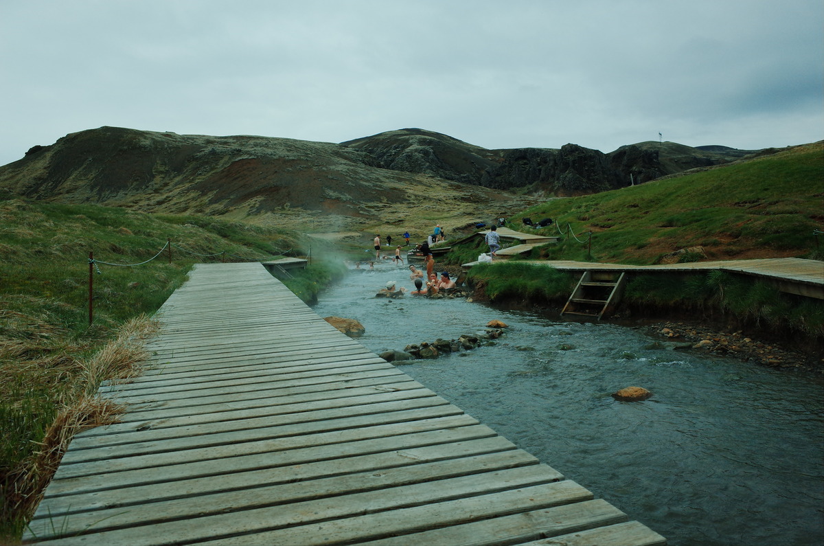 Groups of people bathing in a shallow river with board walk.