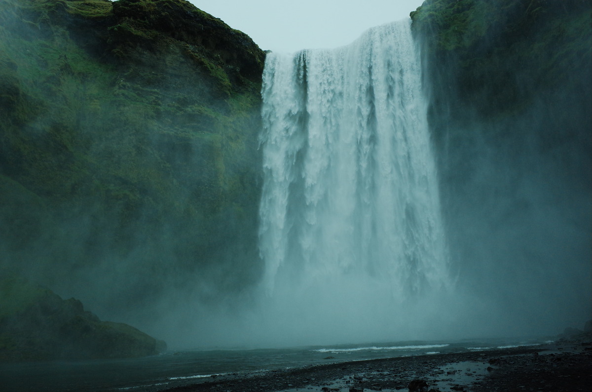 The Skogafoss waterfall plunging into a pool below, surrounded by green mossy cliffs.