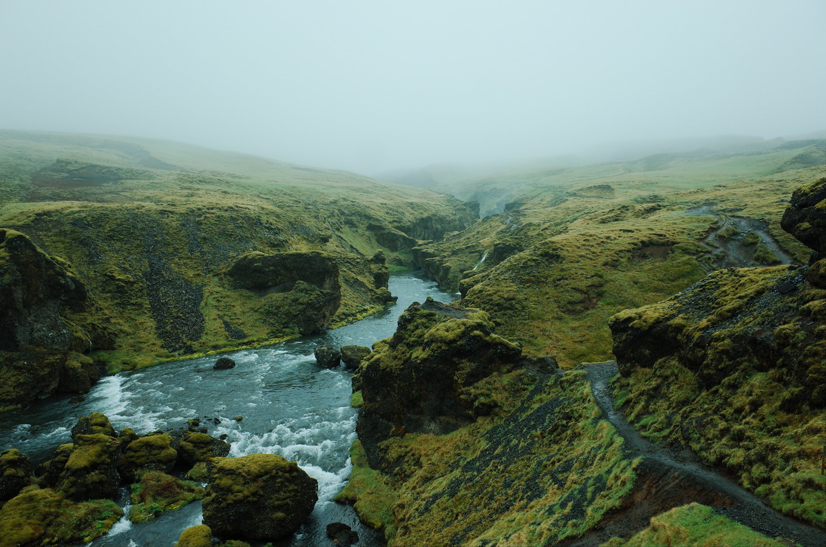 A hiking trail beyond the Skogafoss waterfall, surrounded by lush green hills.