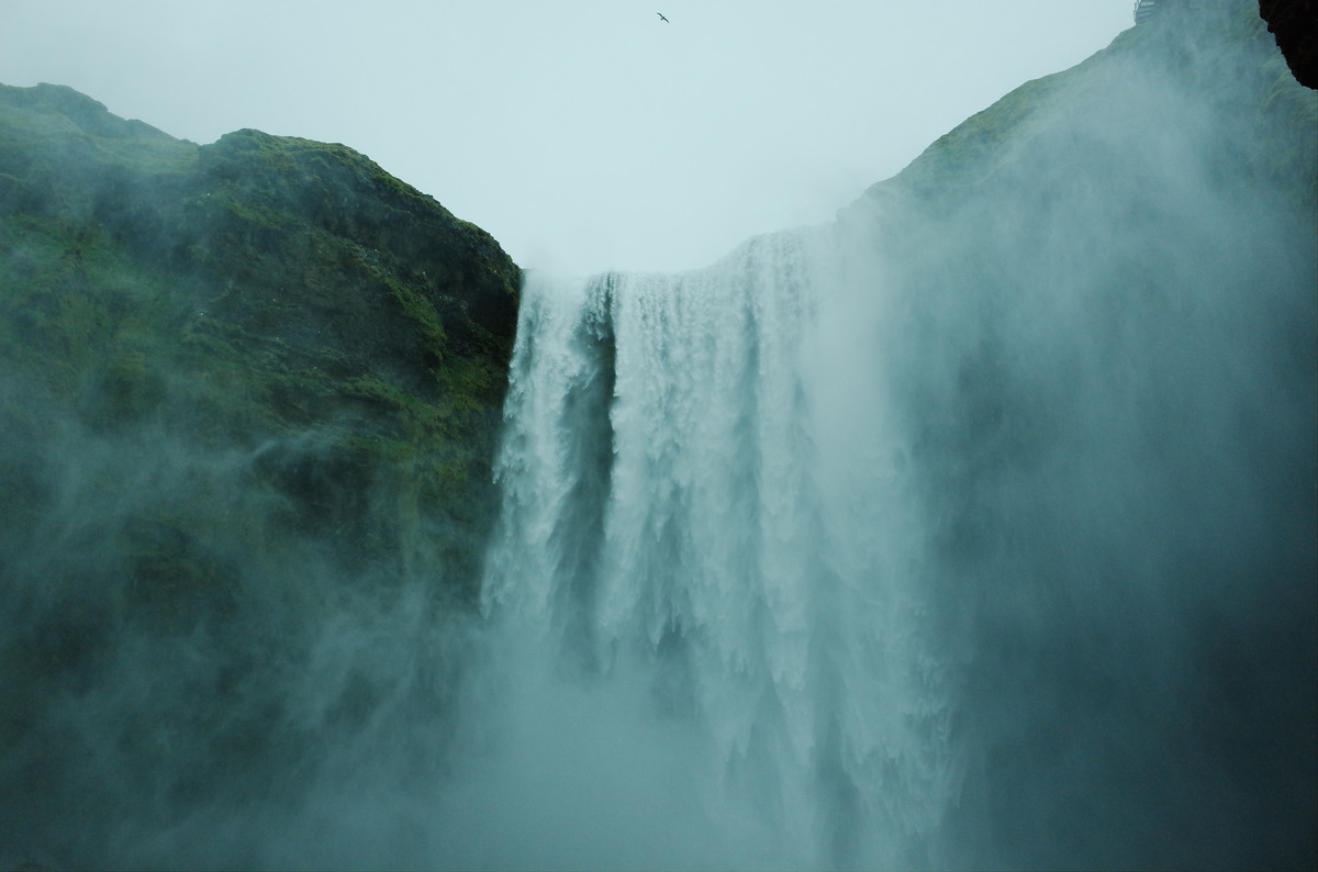 A dramatic upward view of the Skogafoss waterfall cascading down a sheer cliff.