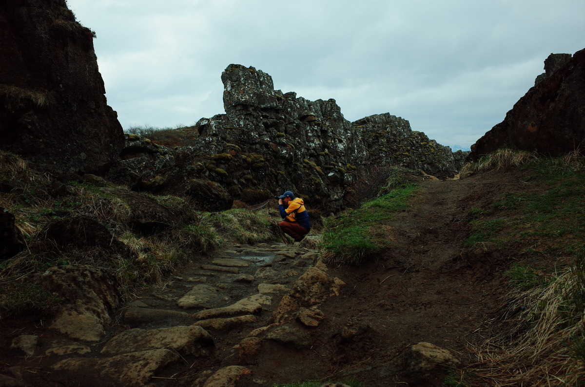 A crouched person with a camera in a fault line of Þingvellir National Park.